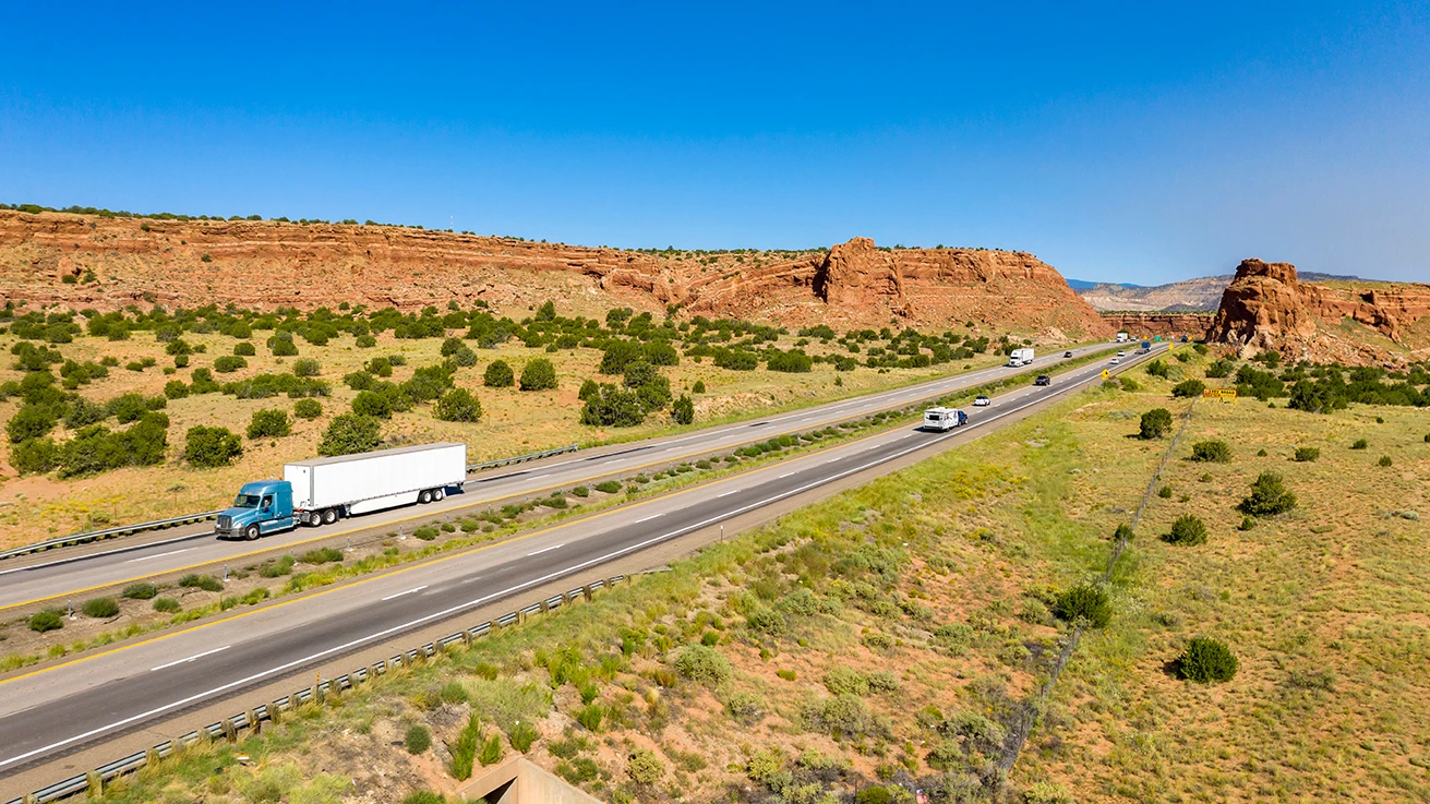 Semi-truck driving on an Arizona highway through red rock desert landscape under clear blue sky