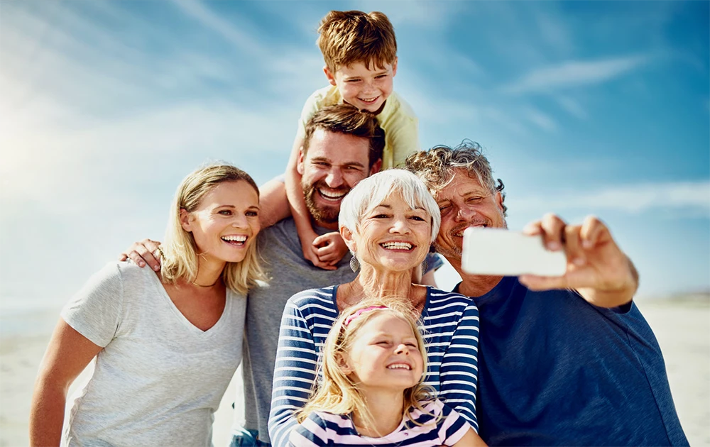 Smiling multigenerational family taking a selfie on the beach, representing connection and family legacy for estate planning.