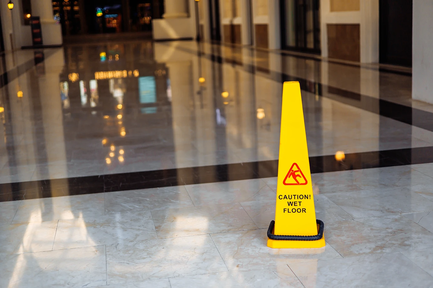 Yellow caution wet floor sign placed on a shiny marble floor inside a commercial building hallway.