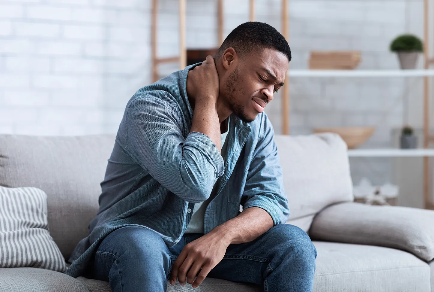 Man holding his neck while experiencing pain at home