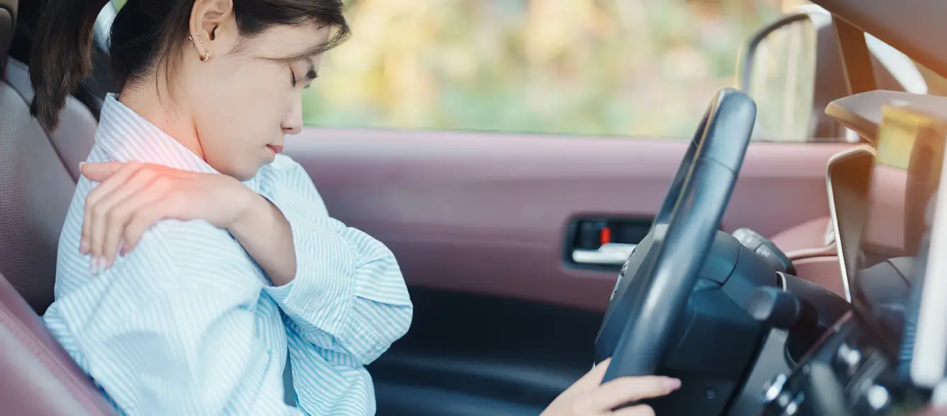 Woman experiencing shoulder pain inside a vehicle after a car accident