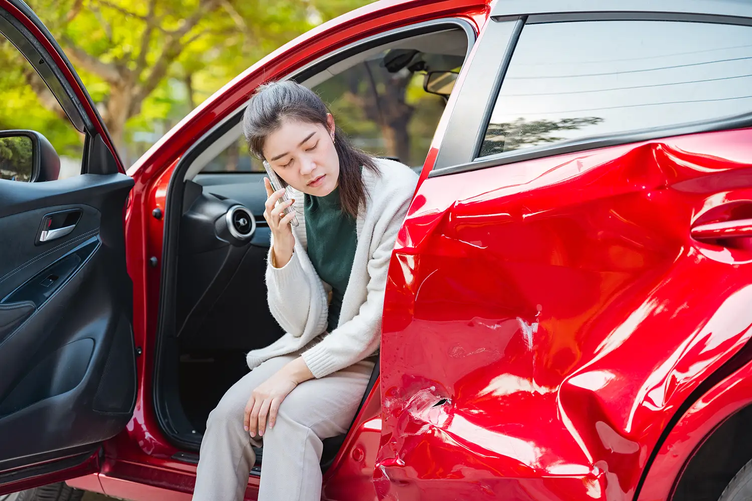Woman sitting in a damaged car after an accident while talking on the phone