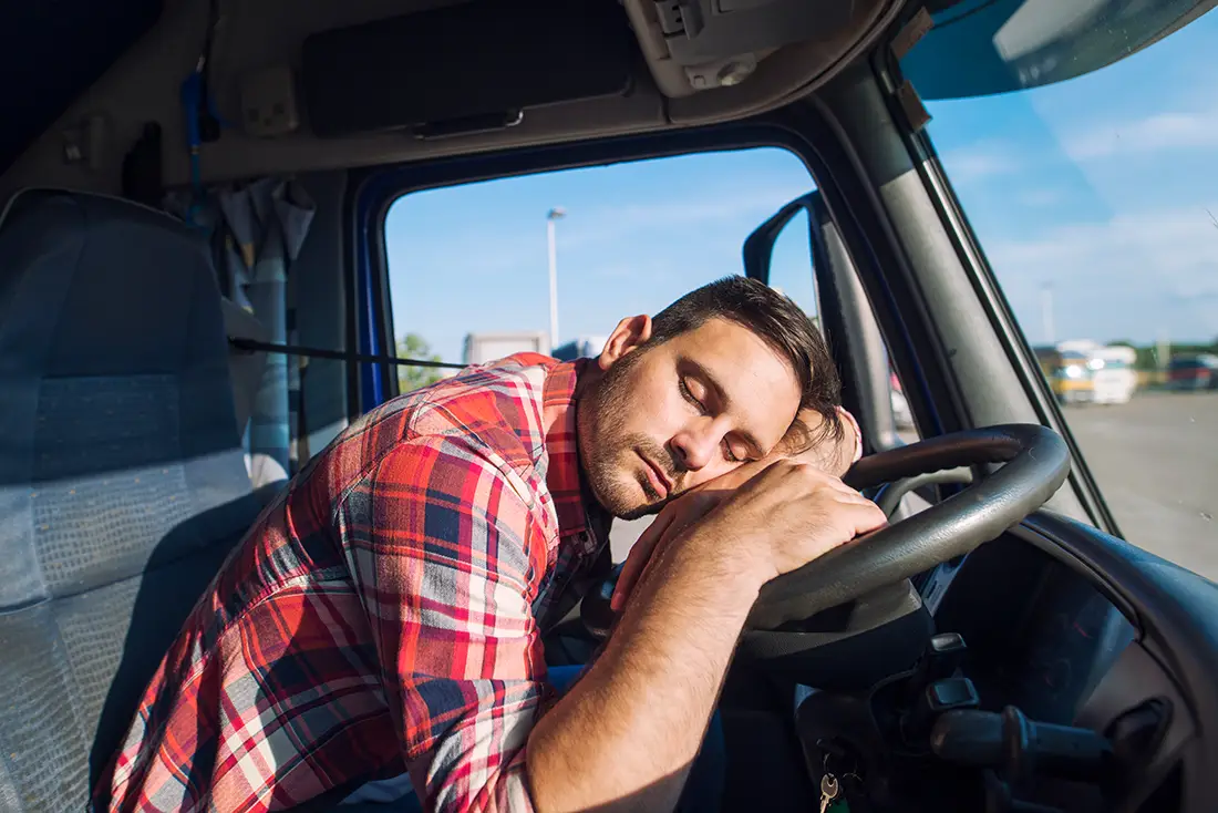 Exhausted commercial truck driver resting his head on the steering wheel after long hours on the road