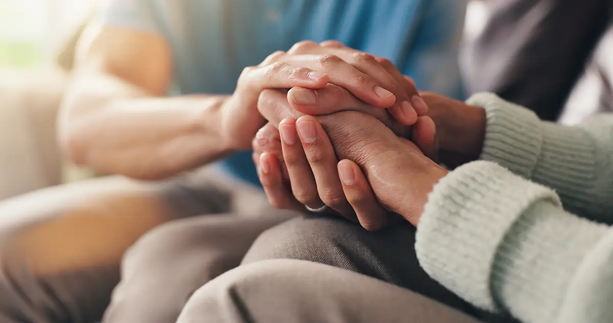 Family members holding hands in comfort and support while coping with the loss of a loved one.
